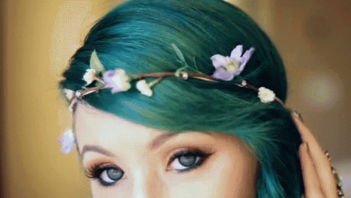 a woman with green hair is wearing a flower crown in her hair