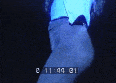 a man in a blue shirt is dancing in a dark room with a clock behind him that says 10:44 .