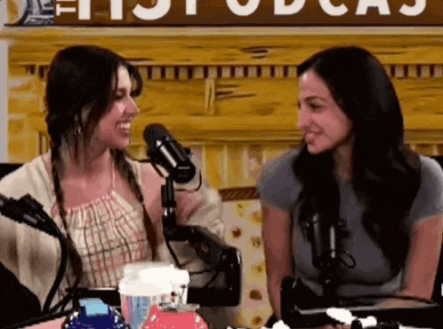 two women are sitting in front of microphones in front of a sign that says podcast .