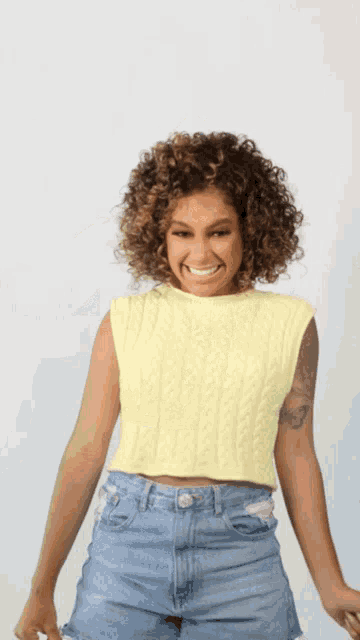 a woman wearing a yellow tank top and blue shorts is laughing