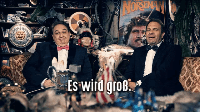 two men are sitting in front of a poster for norsemen