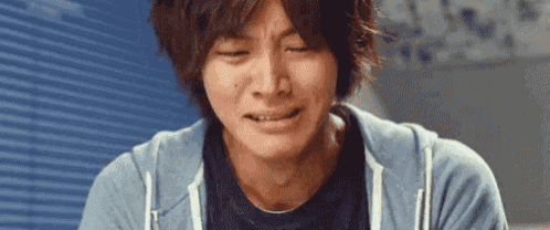 a man in a blue hoodie is crying with his eyes closed and his mouth open .