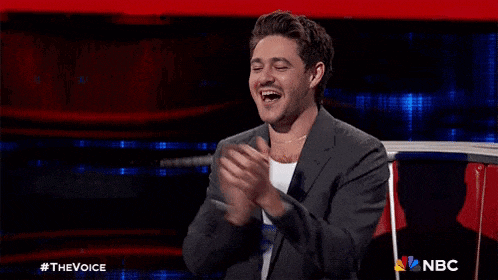 a man in a suit is sitting on a stage with his arms outstretched and smiling .