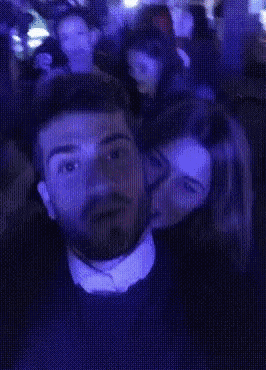 a man with a beard is being kissed by a woman in a crowded room