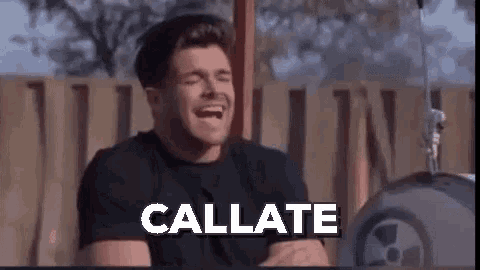 a man is laughing while sitting in front of a drum set with the words callate written on the screen .