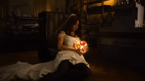 a woman in a wedding dress is holding a pumpkin on her lap