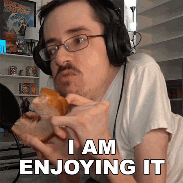 a man wearing headphones eating a sandwich with the words i am enjoying it written below him