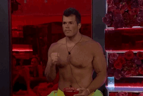 a shirtless man is holding a bowl of food in front of a red wall of roses