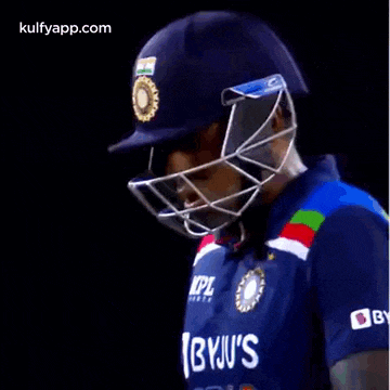 a cricket player wearing a helmet and sunglasses is looking down .