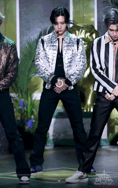 a man in a silver jacket stands on a stage with other men