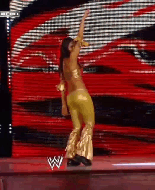 a woman in a gold outfit is dancing on a stage with a w logo in the background