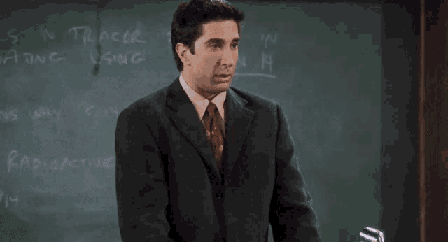 a man in a suit and tie stands in front of a chalkboard that says " s in tracer "