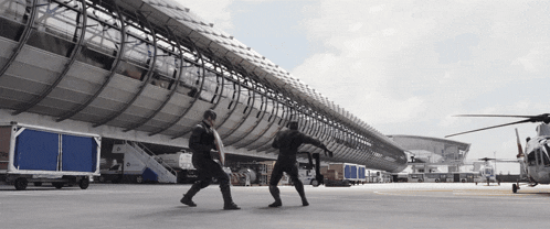 two men are standing on a runway in front of a large building .