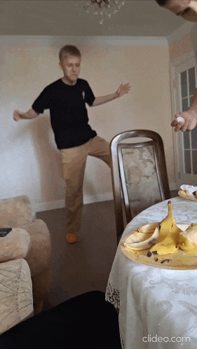 a man in a black shirt is dancing in front of a table with a banana peel on it
