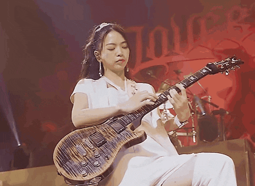 a woman is playing a guitar in front of a sign that says ' tour ' on it