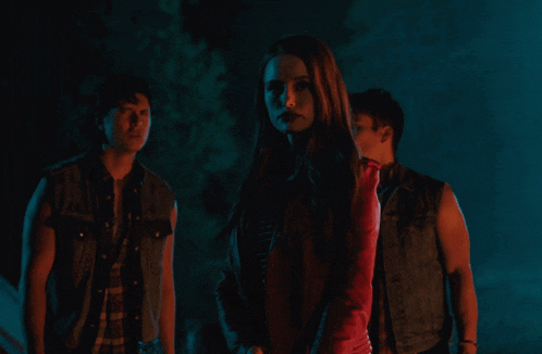 a woman in a red jacket is standing between two men in a dark room