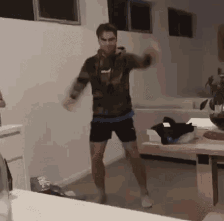 a man is dancing in a living room in front of a table and a window .