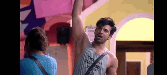 a man in a tank top is standing in front of a woman and raising his arm in the air .