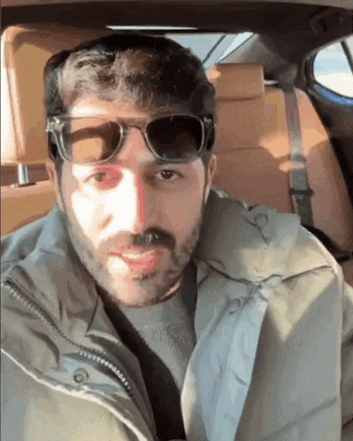 a man wearing sunglasses and a jacket is sitting in the back seat of a car .