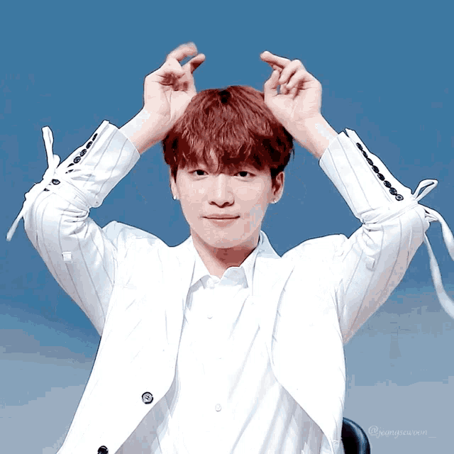a young man making a heart with his hands while wearing a white jacket