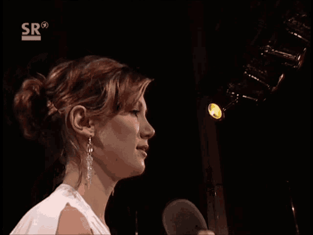 a woman stands in front of a microphone with sr on the bottom right