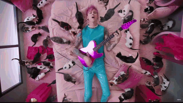 a man is laying on a bed surrounded by cats while playing a guitar