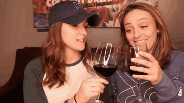 two women are toasting with wine glasses and one is wearing a hat that says ' aa ' on it
