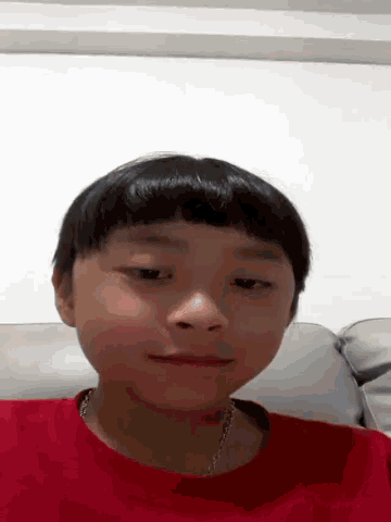 a young boy wearing a red shirt is sitting on a couch .