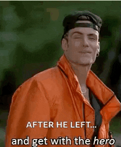 a man wearing an orange jacket and a baseball cap is standing next to a tree .