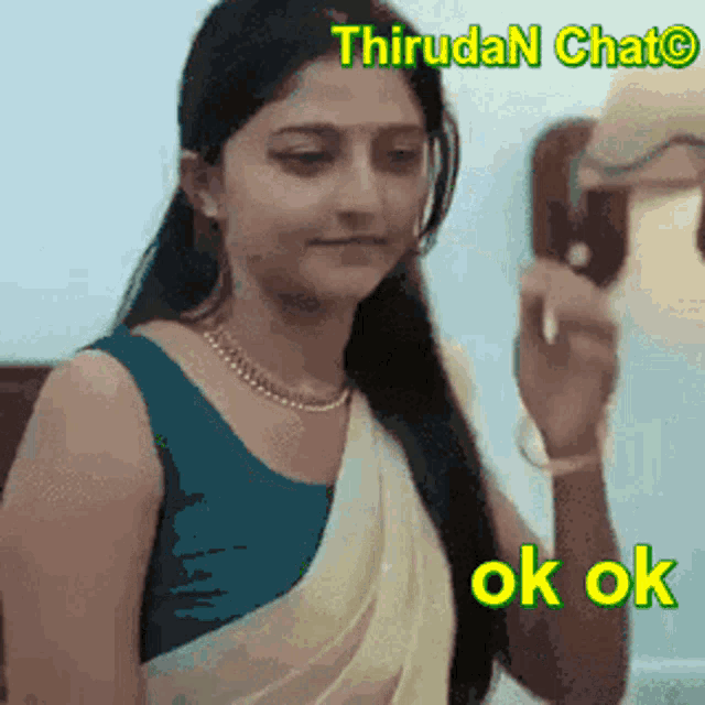 a woman in a blue top and a white saree is talking on a phone with the words ok ok below her