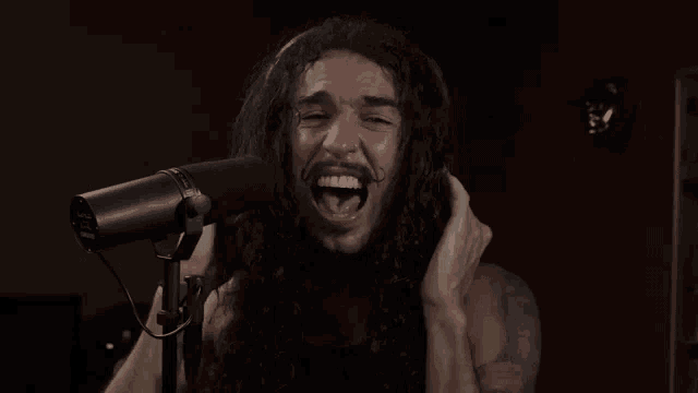 a man with long hair and a beard is singing into a microphone in a dark room .