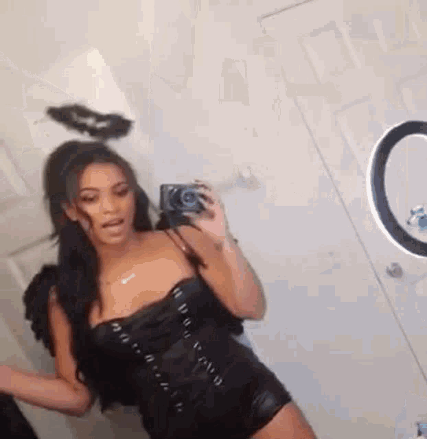 a woman in a black angel costume is taking a selfie in front of a mirror .