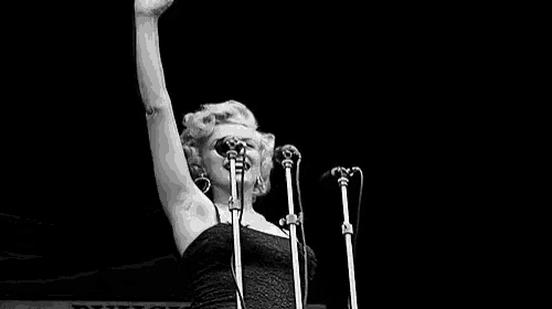 a black and white photo of marilyn monroe singing into a microphone on stage .