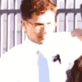 a man wearing glasses and a tie is standing in front of a fence