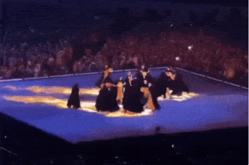 a group of people are dancing on a stage in front of a crowd in a stadium .
