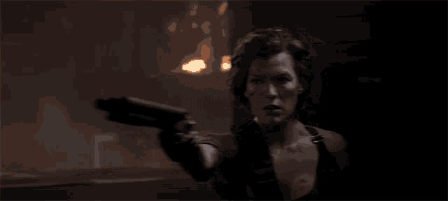 a woman is holding a gun in a dark room and pointing at the camera .