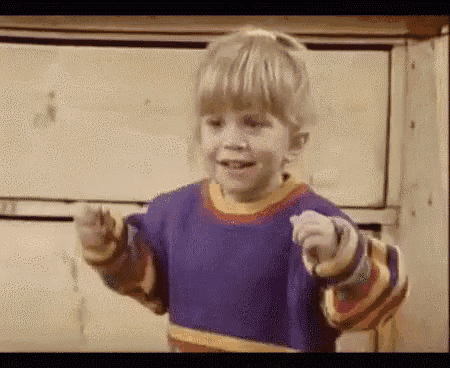 a little girl is wearing a purple sweater and pointing at the camera .