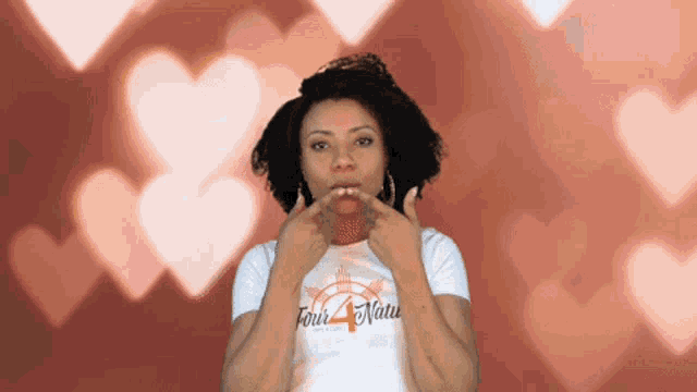 a woman wearing a white shirt that says four natu is making a kissing gesture .