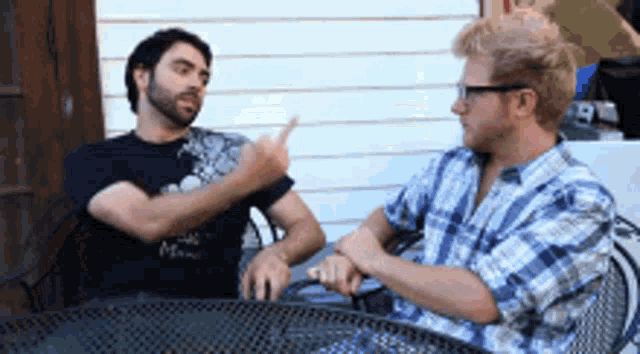 two men are sitting at a table and one of them is pointing