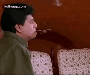 a man is sitting on a couch smoking a cigarette with a fork in his mouth .