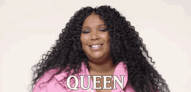 a woman with curly hair is wearing a pink jacket and smiling with the word queen behind her .