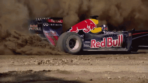 a red bull race car is driving through a dirt field
