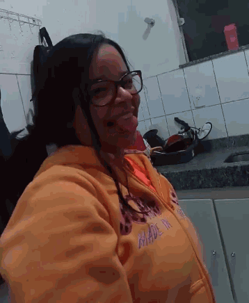 a woman wearing glasses and an orange hoodie that says " made in " sticking her tongue out