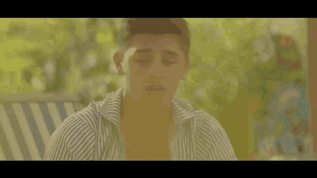 a young man wearing a striped shirt is sitting in a chair with his eyes closed
