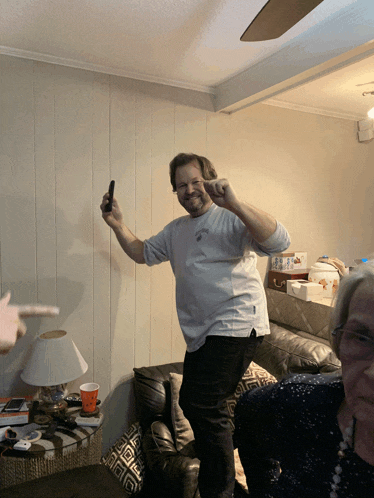 a man standing in a living room holding a cell phone and pointing