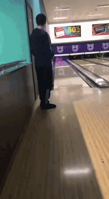 a man standing in a bowling alley with a 50 % off sign on the wall behind him