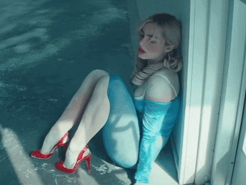 a woman in a blue bodysuit and red heels is sitting on the floor