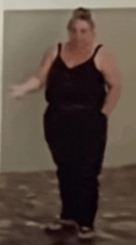 a woman in a black tank top and black pants is standing in a room with her hands in her pockets .