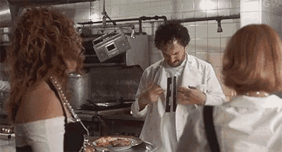 a man is standing in a kitchen talking to two women while a radio is hanging from the ceiling .