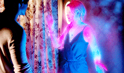 a woman in a blue dress is standing next to a man in a white shirt in a dark room .
